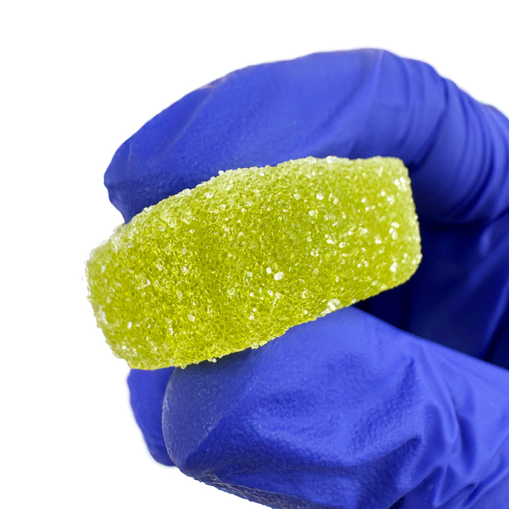 Gummies au THC verts goûts fraise tenu dans une main sur fond blanc